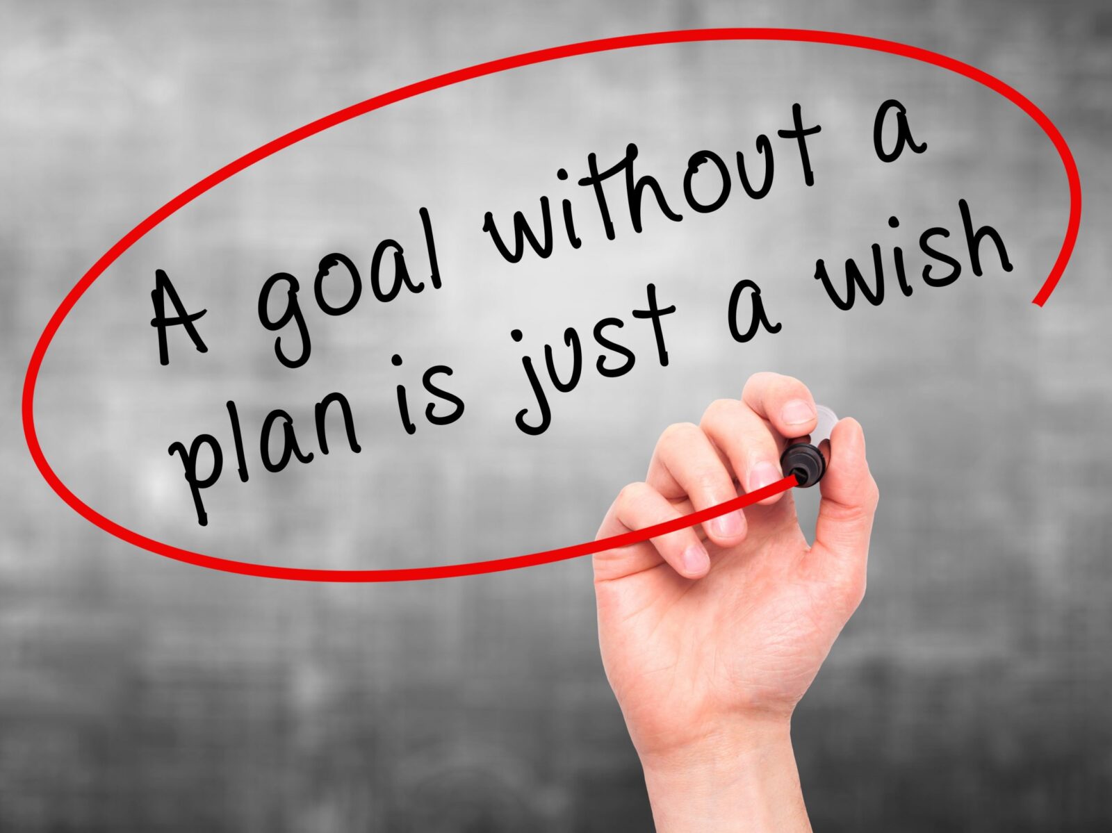 Man Hand writing "A goal without a plan is just a wish" black marker on visual screen.  Business, technology, internet concept.